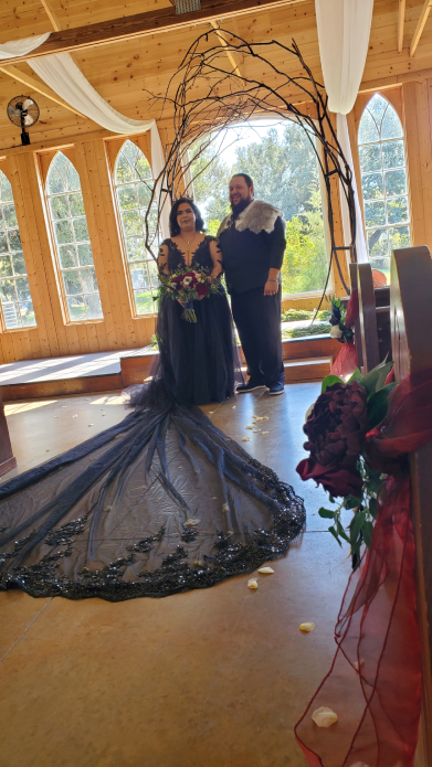 Bride and groom in Viking-inspired black wedding attire standing under wooden ceremonial arch