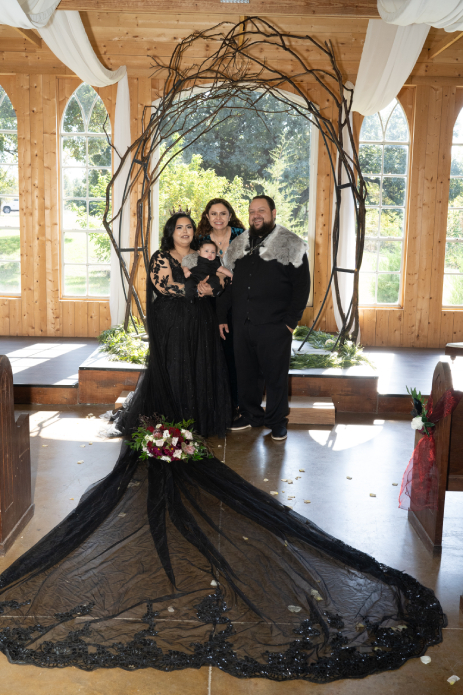 Viking wedding couple and oficiant posing under wooden ceremony arch with floral accents